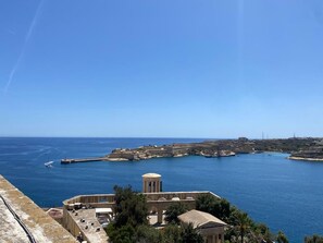 Vista costera con cielo despejado, un edificio histórico con columnas y mar tranquilo.