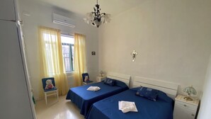 A bedroom with two beds, a chair, a nightstand, and a window with curtains. - Valletta Majestic Grand Harbour View 3-Bedroom by Malta Weekend (Valletta)
