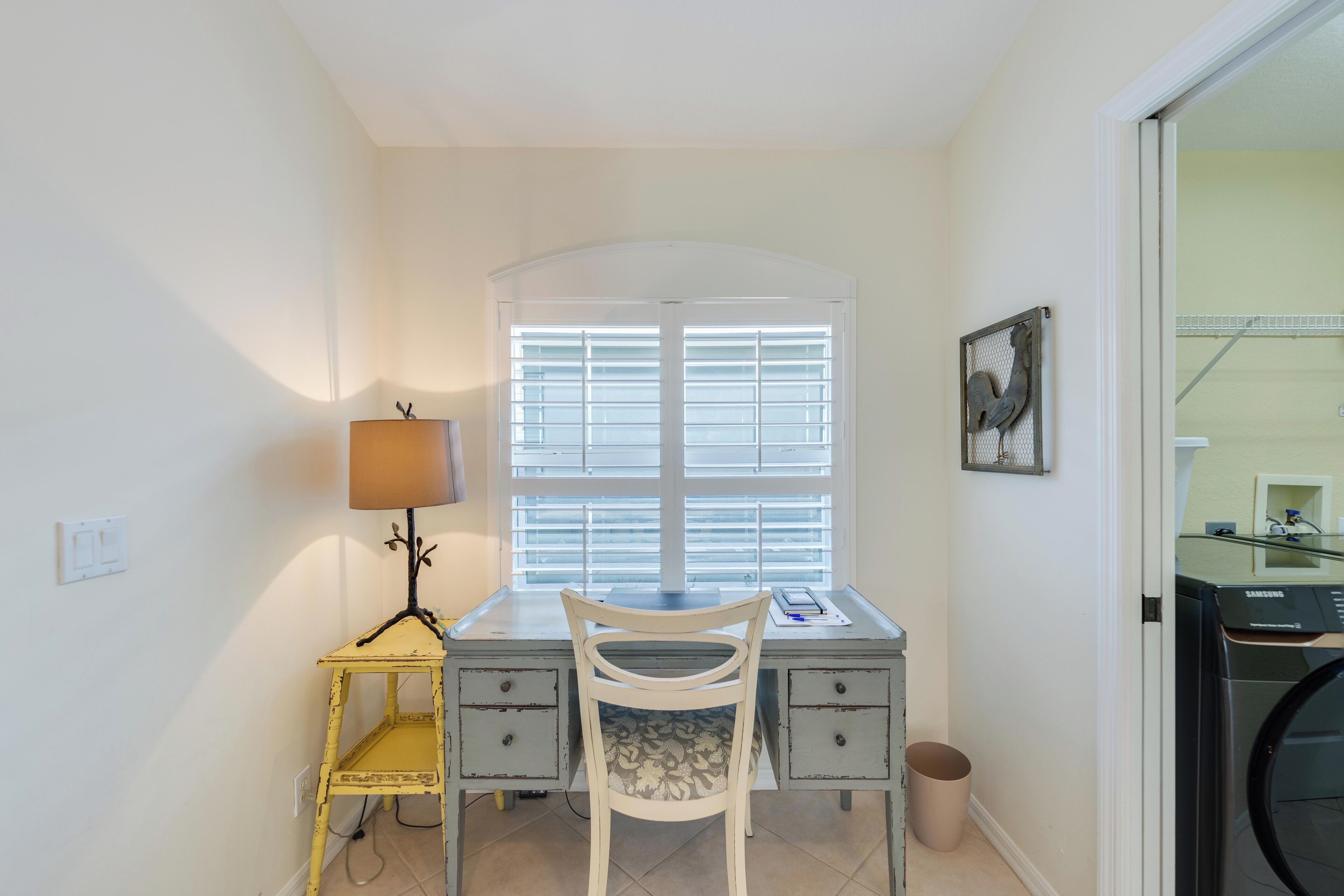 Habitación pequeña con escritorio, silla, lámpara y lavadora.