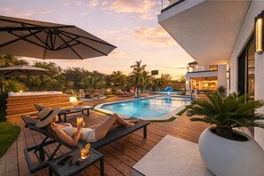 A poolside area with lounge chairs, a hot tub, and a modern building in the background. - Lux Resort • Pool_Spa_Gym • Near Hard Rock Stadium (Hialeah)