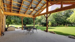 Een overdekt terras met een tafel en stoelen, omgeven door een natuurlijke omgeving.