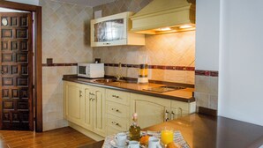 A kitchen with wooden cabinets, a microwave, a sink, and a breakfast tray with coffee cups, a muffin, and orange juice. - LA CASA DEL MAESTRO DE MÚSICA (Baeza)