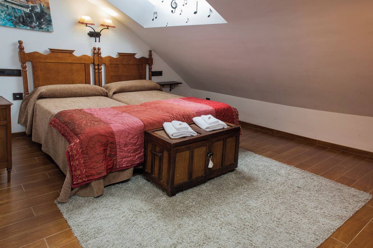 Une chambre avec deux lits, une tête de lit en bois, une table de chevet, une lampe et une lucarne décorée de notes de musique.