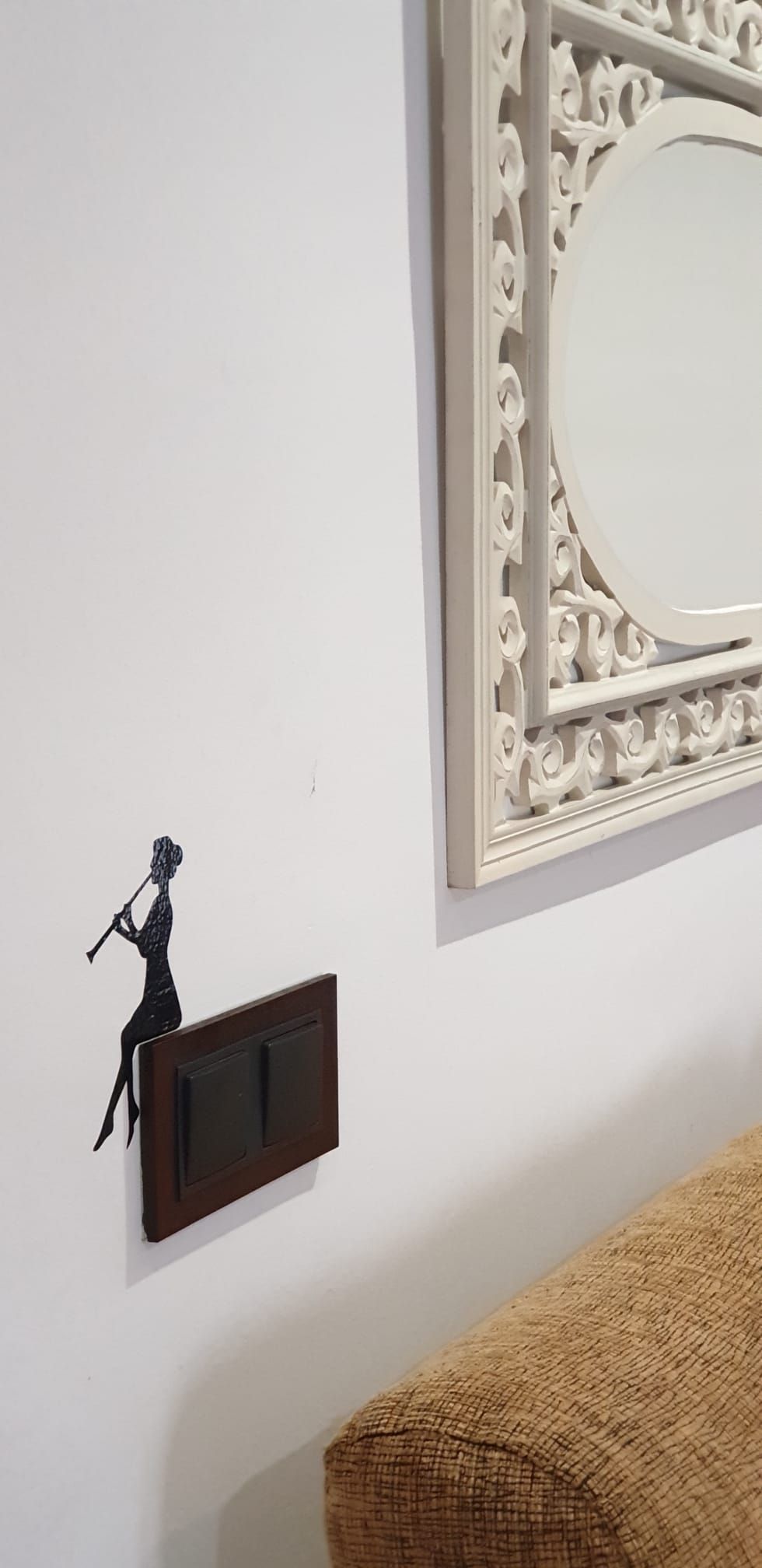 A wall-mounted light switch, a decorative wall panel, and a portion of a brown couch.