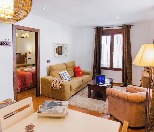 Un salon avec un canapé, une petite table sur laquelle se trouve un ordinateur portable, une lampe et une fenêtre avec des rideaux.
