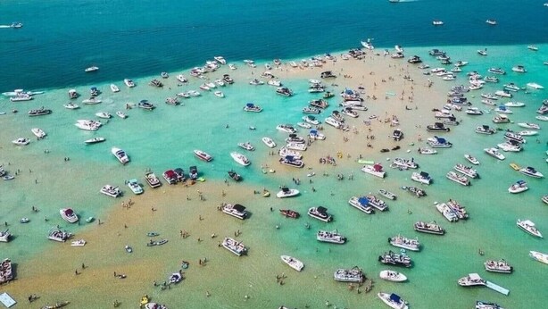 Luchtbeeld van een strand met veel boten en mensen.