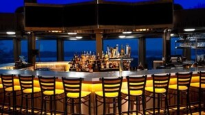 Een bar met een lange toonbank, meerdere krukken en uitzicht op de zee in de schemering.