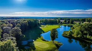 Een golfbaan met een meer, omgeven door dichte bomen en een heldere lucht.