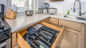 Una cocina con armarios de madera, una encimera, un fregadero, un tostador, una licuadora y un organizador de cajones con utensilios.