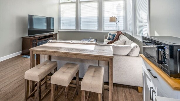 Una sala de estar moderna con una mesa de comedor de madera, asientos tipo banco, un sofá, un televisor y un microondas.