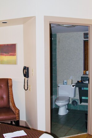 A hotel room with a brown leather chair, a telephone, and a toilet visible through an open door. - Spacious lodge with 18 bedrooms, large living area with pool table and more! (Tulsa)