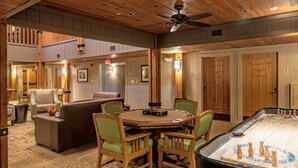 Um quarto acolhedor com teto de madeira, um ventilador de teto, uma mesa redonda com cadeiras e uma mesa de futebol.