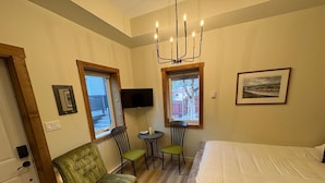 Ein Zimmer mit einem Bett, einem grünen Sessel, zwei Stühlen, einem kleinen Tisch, einem Fernseher und einem Fenster mit Blick.