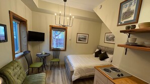 Ein kleines Schlafzimmer mit Bett, einer kleinen Küchenzeile, einem Esstisch, einem grünen Sofa und einem Fernseher.