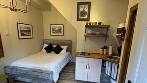 Ein gemütliches Schlafzimmer mit Bett, Nachttischen, einer kleinen Küchenzeile und einem Badezimmer.