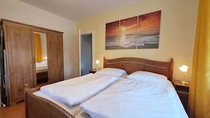 A double bed with white linens, a wooden headboard, two bedside lamps, and a sunset painting on the wall. - Comfortable, very quiet and sunny apartment. Only 5 minutes to the Silbersee (Villach)
