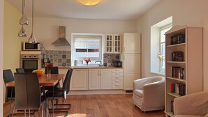 A modern kitchen with white cabinets, a dining table with chairs, a bookshelf, and a window with a view. - Comfortable, very quiet and sunny apartment. Only 5 minutes to the Silbersee (Villach)