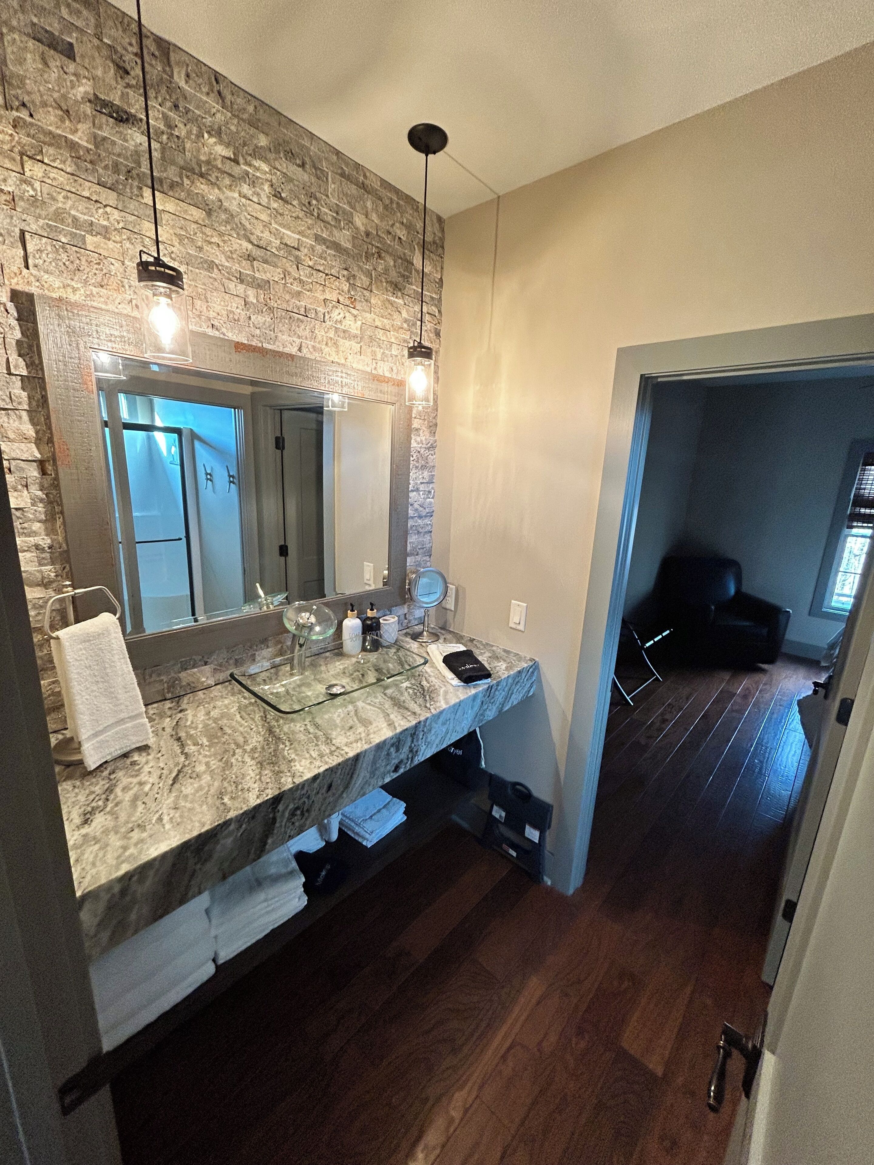 A bathroom with a marble countertop, a large mirror, and a hanging light fixture.