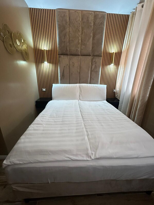 Un lit bien fait, avec une tête de lit, deux tables de chevet et des panneaux décoratifs sur les murs.