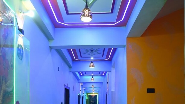 A hallway with a modern design, featuring a geometric ceiling pattern, blue and purple neon lighting, and a central light fixture. - HOTEL NIRVANA INN (Rajgir)