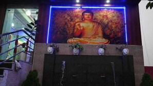 A Buddha statue with a blue neon frame, a staircase, and a water feature. - HOTEL NIRVANA INN (Rajgir)