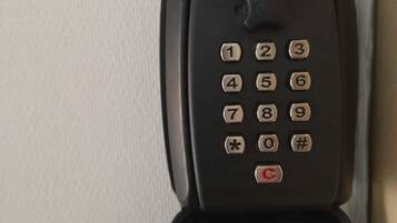 A black telephone with a numeric keypad and a red "C" button, placed against a white wall.