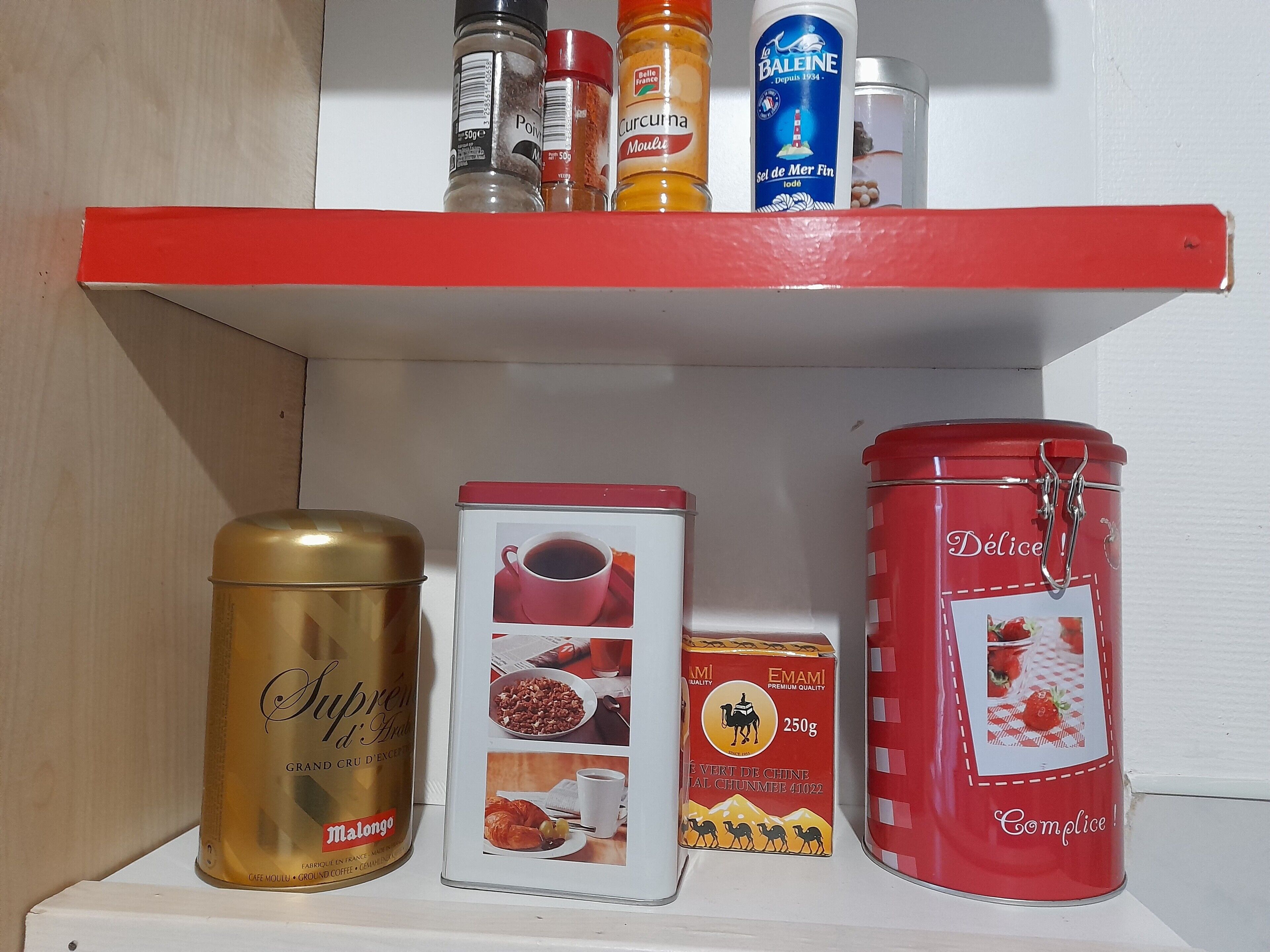 A shelf with various food items including a can of coffee, a jar of spices, and a tin of chocolate.