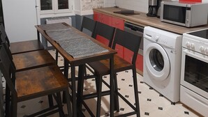 A compact kitchen with a dining area, featuring a washing machine, microwave, and red cabinets. - Sweet Home Appartement 2 chambres séparées, 3 lits proche du centre ville (Cholet)