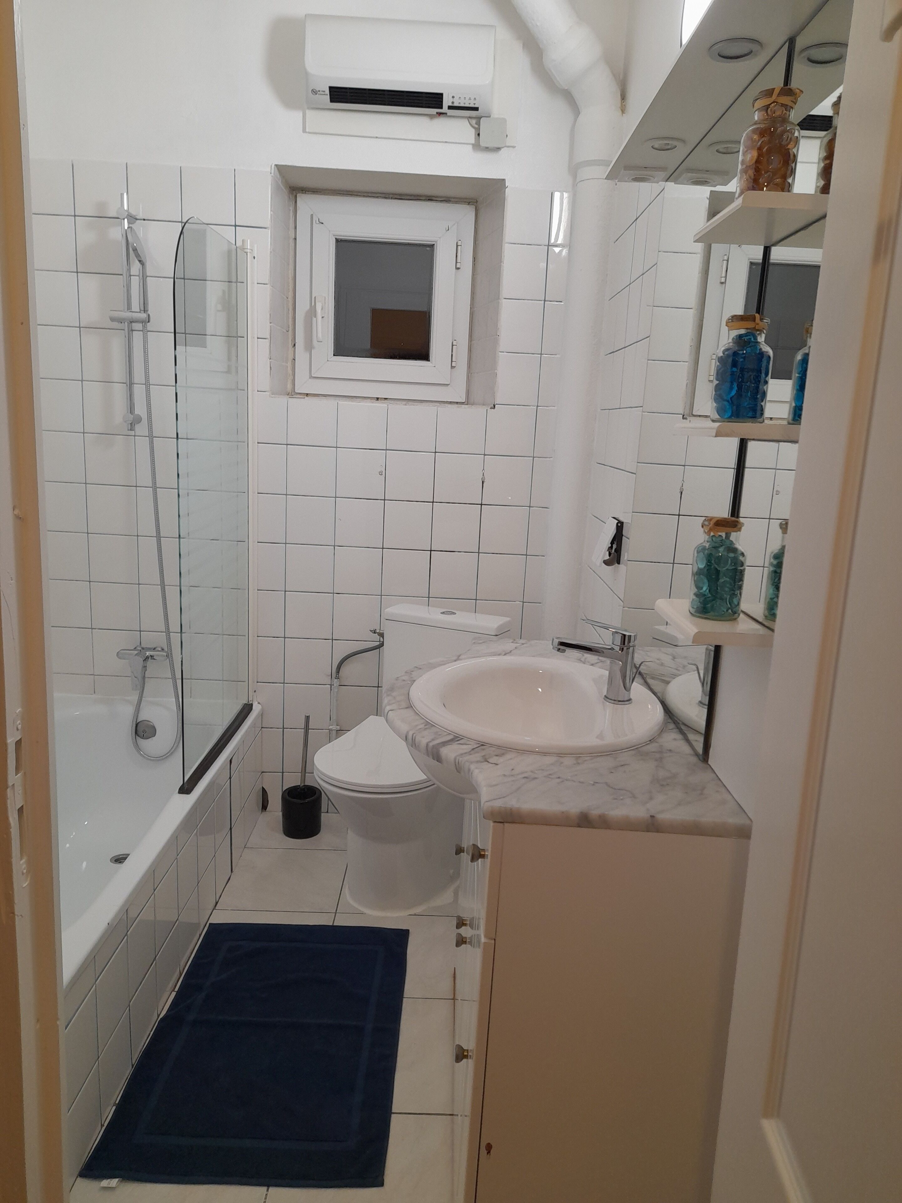 A bathroom with a shower, toilet, sink, and a small window.