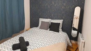 A bedroom with a patterned bedspread, a dark headboard, a mirror, and a radiator. - Sweet Home Appartement 2 chambres séparées, 3 lits proche du centre ville (Cholet)