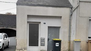 A building with a grey facade, a white door, and a small window. There are two trash bins outside, one with a yellow lid. - Sweet Home Appartement 2 chambres séparées, 3 lits proche du centre ville (Cholet)