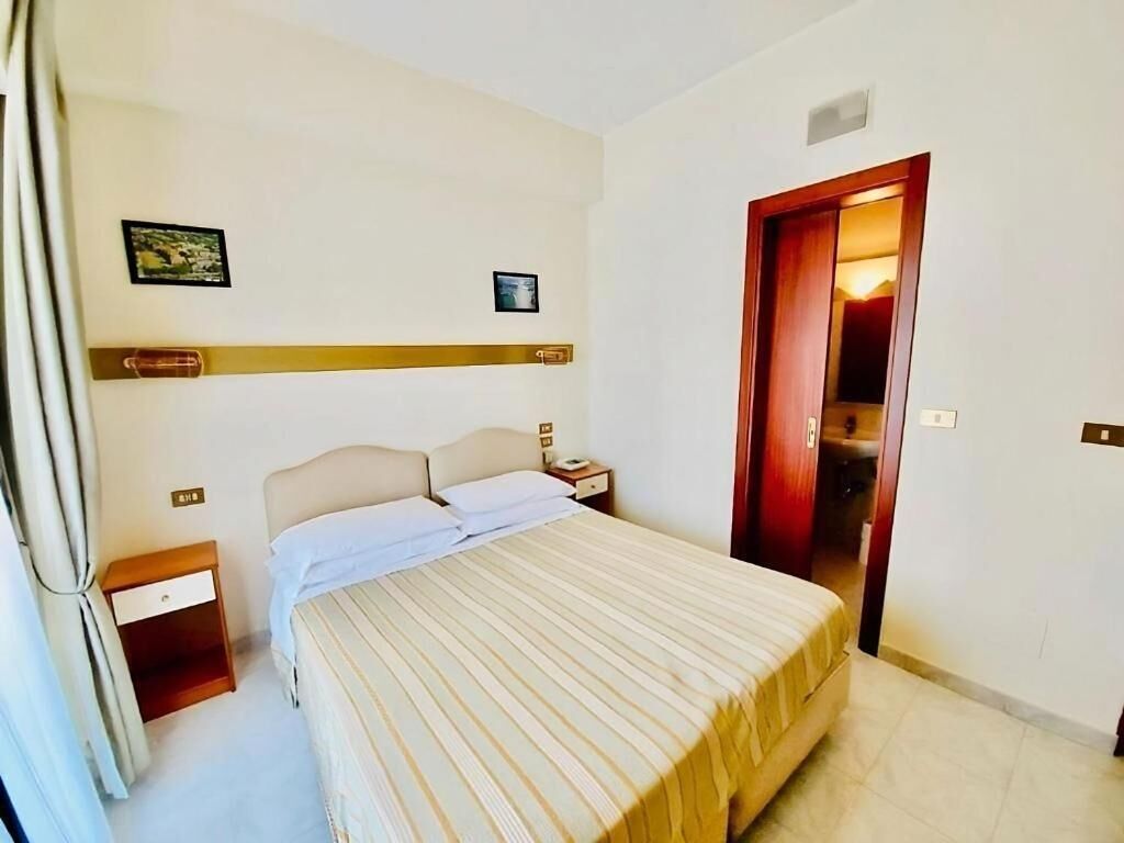 A bedroom with a bed, nightstand, and a door leading to another room.