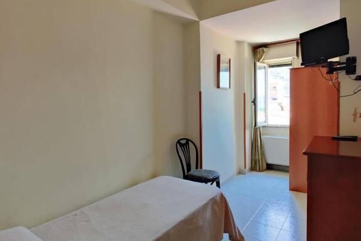 A room with a single bed, a chair, a desk with a television, and a door leading outside.