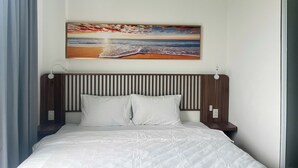 A hotel room with a bed, a headboard, a nightstand, and a wall-mounted painting of a beach scene. - Triland Hillside (Phu Quoc)