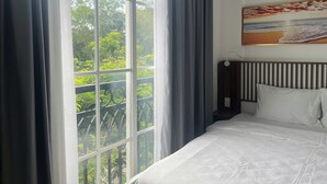 A hotel room with a large window, a bed with white bedding, and a painting on the wall. - Triland Hillside (Phu Quoc)