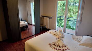 A hotel room with a large bed, a mirror, a chair, a small table, and a balcony with a view of trees.