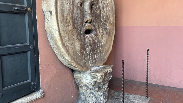 A stone sculpture with a face, a black door, and a herringbone-patterned floor. - Alice's apartment 1 (Roma)