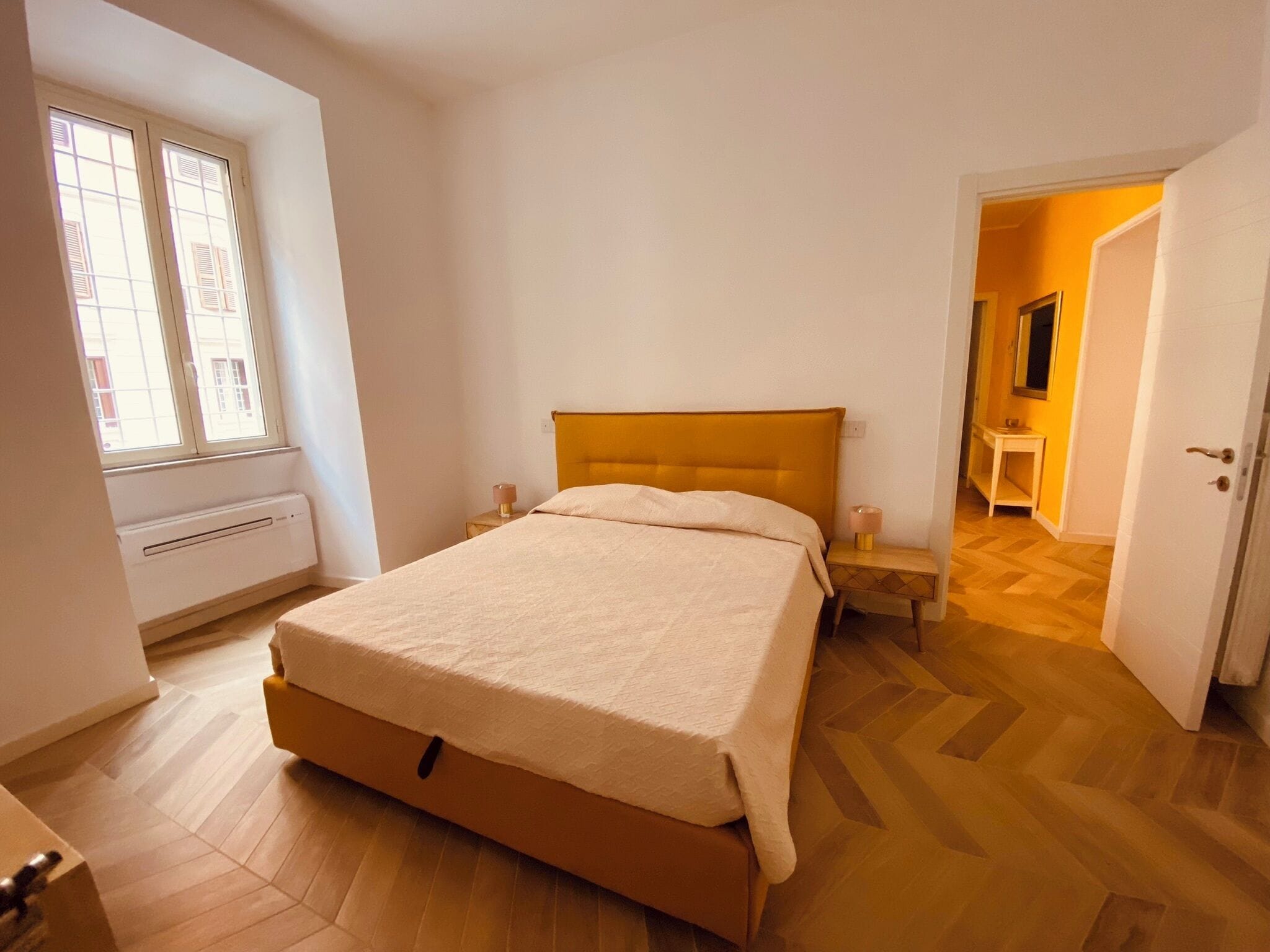 Una camera da letto con un letto, comodini, una finestra e una porta che dà su un'altra stanza.