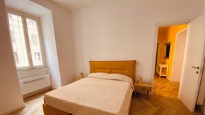 A bedroom with a bed, bedside tables, a window, and a door leading to another room. - Alice's apartment 1 (Roma)