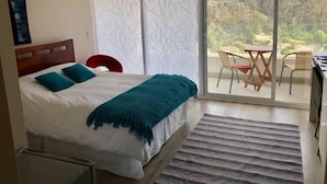 A bedroom with a bed, a view of a balcony with chairs, and a cityscape in the background. - Departamento Centro de viña del mar (Vina del Mar)
