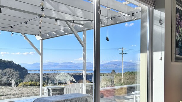 A room with a large window overlooking a scenic landscape, a covered outdoor area, and a chair near the window. - Beautiful 7 BR Home Ring of Kerry - Beach -Golf nearby - Killarney 30 min.drive (Killarney)