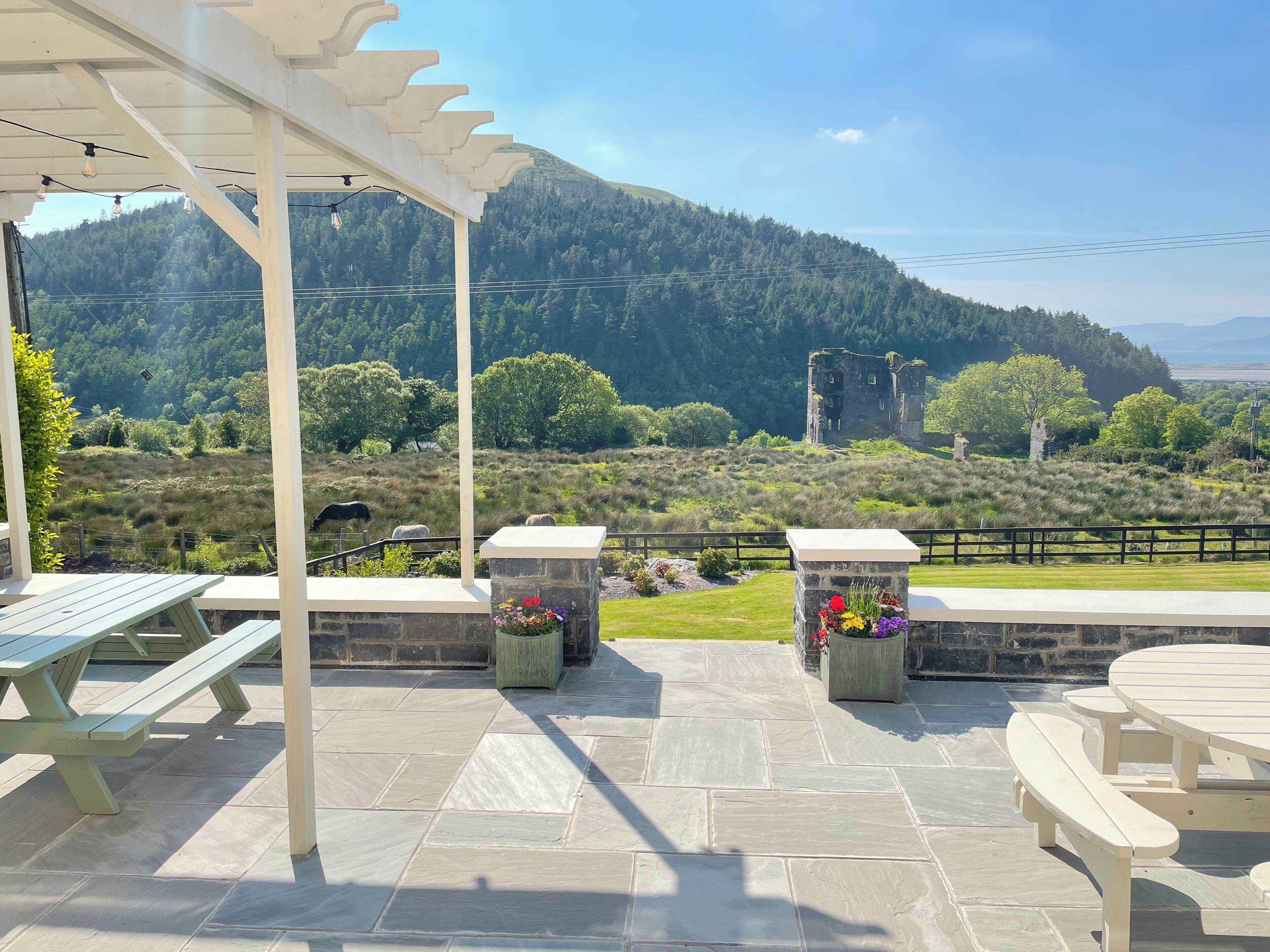 Eine Terrasse im Freien mit Steinboden, Holzbänken und einer Pergola.
