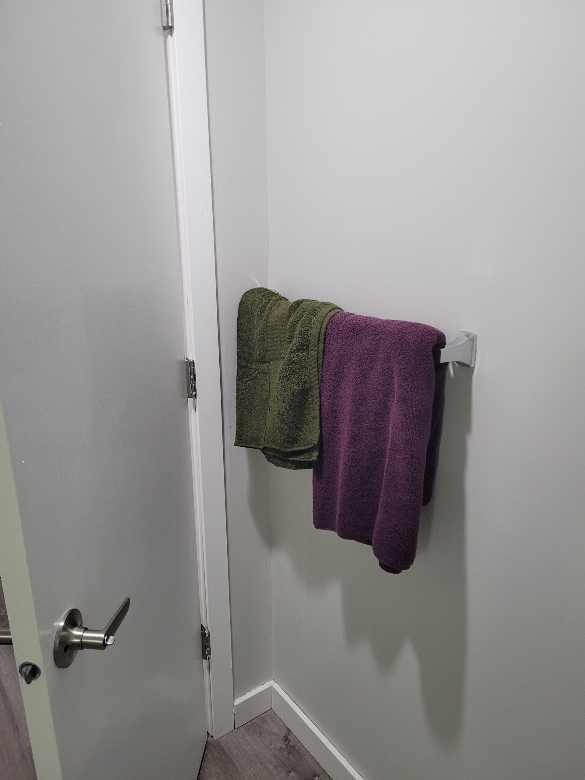 Ein Badezimmer mit einer weißen Tür, einem Handtuchhalter mit einem gr ün-lila Handtuch und Holzboden.