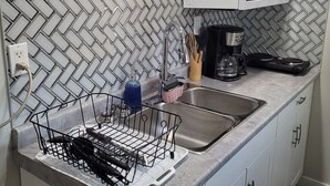 Una cocina con salpicadero de baldosas en espiga, un lavamanos doble, un microondas y un escurreplatos.