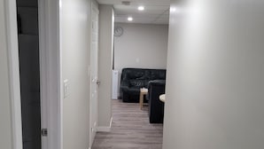 Un pasillo estrecho con piso de madera, paredes blancas y un sofá negro al fondo.
