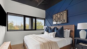 A bedroom with a large bed, a nightstand, a lamp, and a window with blinds.