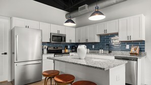 A modern kitchen with white cabinets, stainless steel appliances, a granite countertop, and two wooden bar stools.