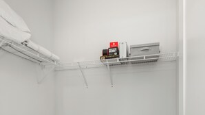 A small, white closet with a hanging rack, shelves, and a storage unit.