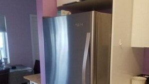 Una cocina con un refrigerador de acero inoxidable, una mesa de comedor con sillas y un armario blanco.