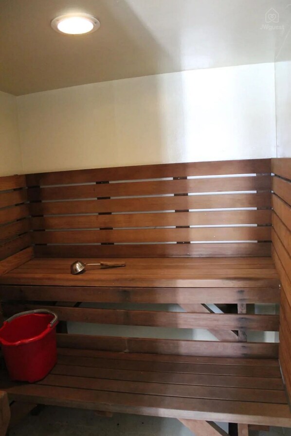 Un banco de madera con un objeto metálico encima y un cubo rojo a su lado.